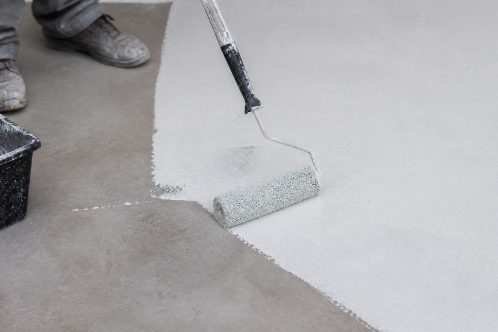 Rouleau appliquant finition blanche deux couches sur beton gris