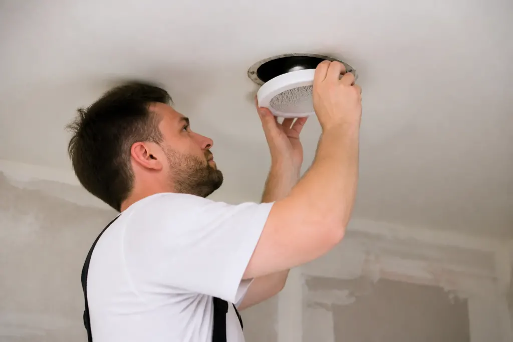 Technicien fixant une grille ronde blanche au plafond