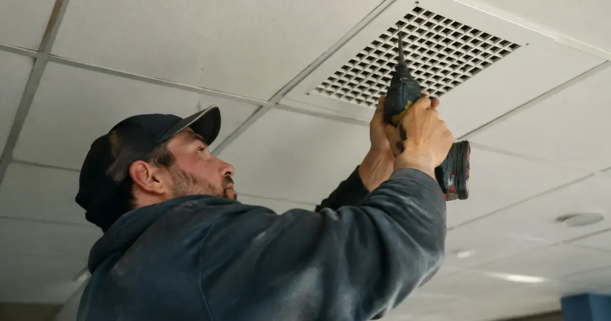 Un technicien visse une grille blanche au plafond carrele